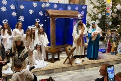 Scena z przedstawienia. Święta rodzina stoi na tle szopki w towarzystwie aniołów.