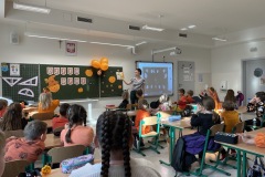 Pani Ilona z uczniami w sali klasowej czyta dzieciom opowiadanie z książki i pokazuje ilustracje