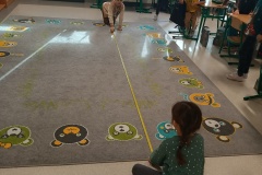 Uczniowie mierzą długość dywanu przy użyciu miarki budowlanej