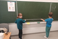 Uczniowie mierzą długość tablicy przy wykorzystaniu miarki drewnianej