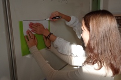 Dwie uczennice rysują na tablicy oś liczbową przy pomocy deski do krojenia.