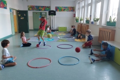 Zabawy z piłka i hula-hop. Uczniowie siedzą, rzucają piłkę do obręczy.