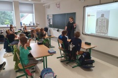 Katarzyna Bobrowska w sali klasowej prezentuje uczniom zdjęcie stroju ludowego wyświetlone na tablicy multimedialnej.