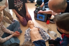 Uczniowie zebrani  wokół fantomu do ćwiczeń obserwują prezentowaną resuscytację