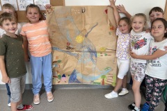 Grupa dzieci z klasy 1b prezentuje swoją prace plastyczną wykonaną na dużym arkuszu szarego papieru z użyciem pasteli olejowych. Praca przedstawia rzekę Niemen i jej otoczenie widziane oczami dzieci.