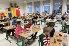 Uczniowie w sali klasowej siedzą przy ławkach podczas pokazu wykonania stroika świątecznego.