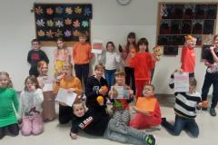 Uczniowie w pomarańczowych koszulkach prezentują ciekawostki o warzywach i owocach